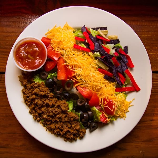 Taco salad with ground beef, shredded cheese, tomatoes, olives, tortilla strips, and salsa.