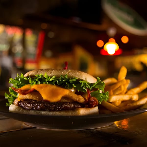 A Wraptitude burger with cheese, bacon, lettuce, and onion rings, served with fries.