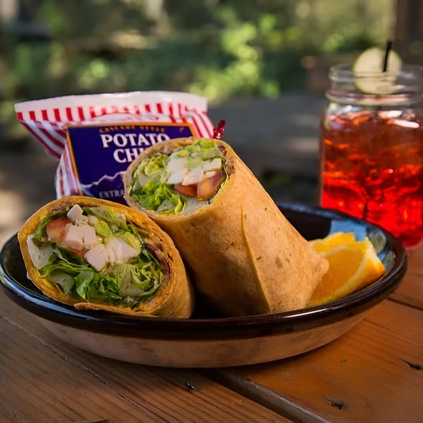 Two Wraptitude wraps with chicken, lettuce, and tomato, served with chips and a drink.